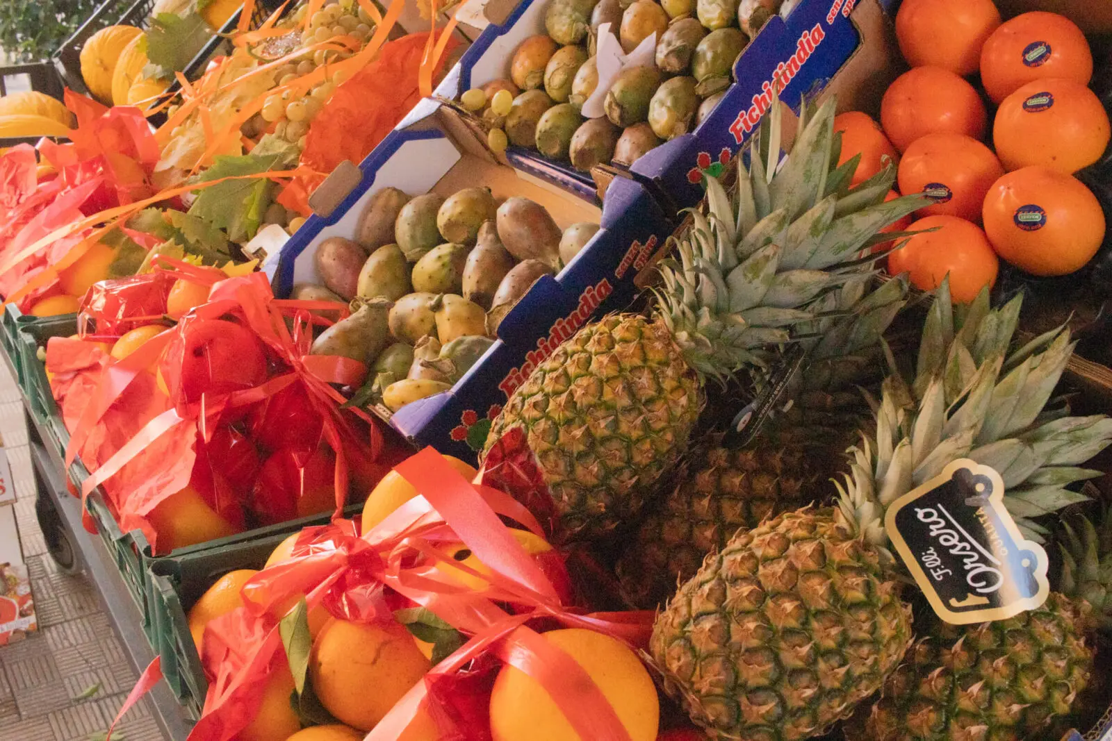 Frutta esotica e agrumi in cassette di legno, decorati con nastri rossi.