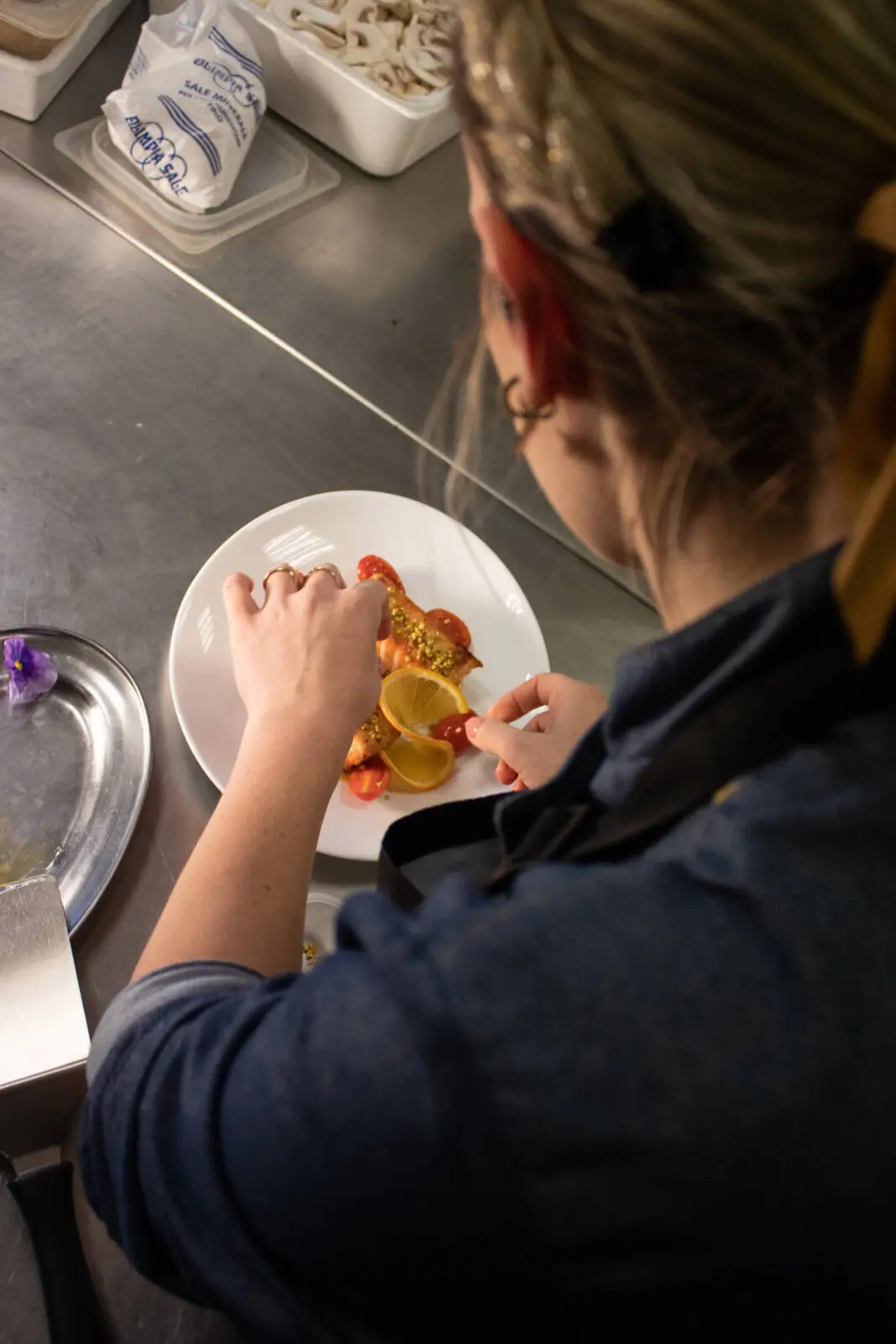 Chef che impiatta piatto di salmone, pomodorini e arancia.